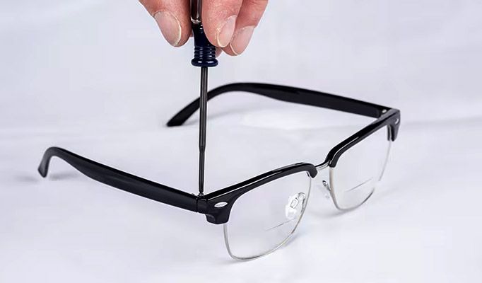 Using a small screwdriver to tighten a screw on a pair of black-rimmed glasses