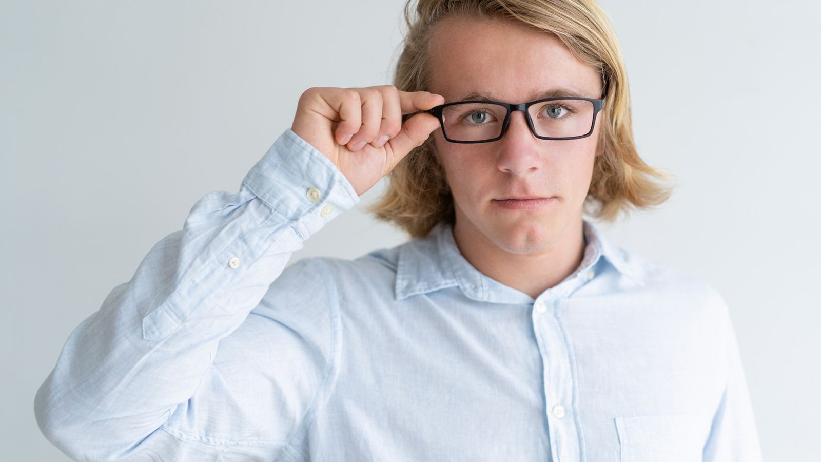 A young man adjusting his black rectangular zero-power plano glasses, suitable for everyday use.