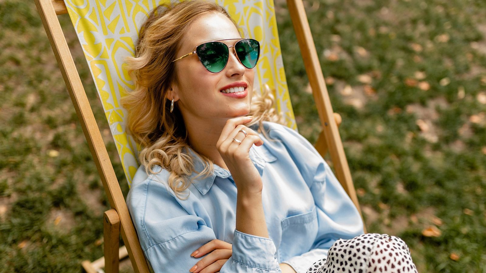 A smiling woman wearing green lens sunglasses relaxes in a deckchair, demonstrating the benefit of reduced eye strain in the sun.