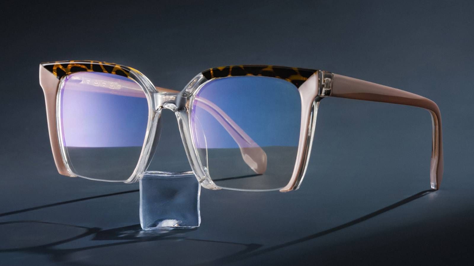 Close-up of a pair of clear-framed blue light glasses with tortoise-shell accents on the temples and a slight blue reflection on the lenses