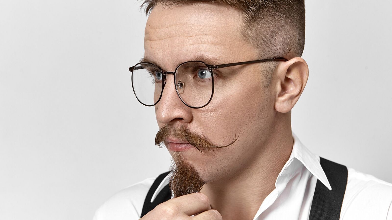 A stylish man with a handlebar mustache wearing round non-prescription plano glasses for fashion.